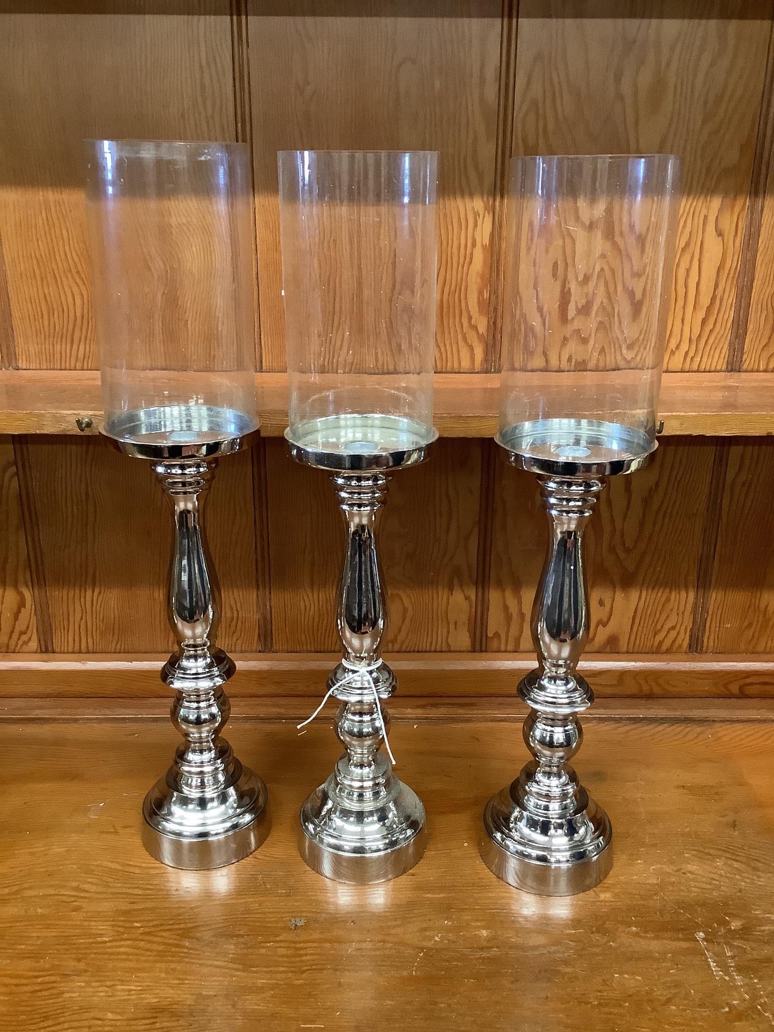 Set of three nickel plated candle stands with glass shades, height 51cm
